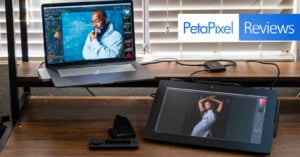 A laptop and a tablet displaying photo editing software are placed on a wooden desk. A man’s portrait is on the laptop screen, while a woman’s portrait is on the tablet screen. Above, the text reads "PetaPixel Reviews." A pair of editing gloves and a control deck are on the desk.