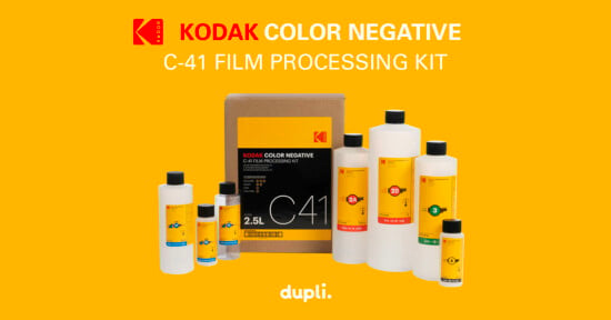 The image shows a Kodak Color Negative C-41 film processing kit, including multiple bottles of chemicals in varying sizes, all against a yellow background. Text on the image reads "Kodak Color Negative C-41 Film Processing Kit" along with the "dupli." logo at the bottom.