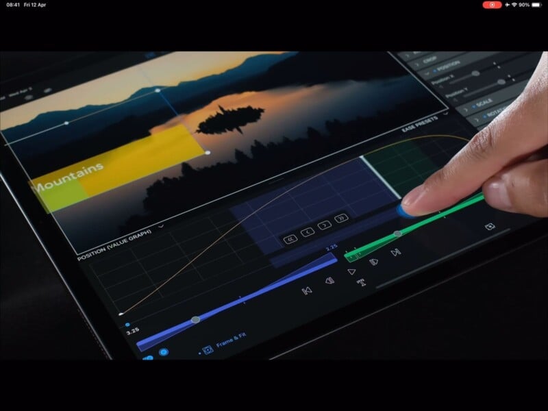 Close-up of a person’s hand using a touch interface on a tablet to edit a video. The screen displays a video editing software with a timeline, color curves, and a preview of a landscape scene featuring mountains and a body of water.