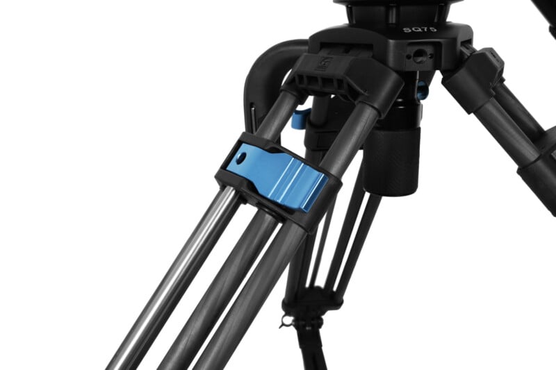 Close-up of a professional camera tripod with a blue adjustment clamp. The black and silver tripod legs have a robust design with the clamp positioned centrally on the legs, used for adjusting height and stability. The model "SGT5" is labeled on the tripod.