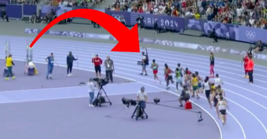 A field scene shows athletes running on a bright blue track during an Olympic event. A large red arrow is superimposed over the image, pointing towards one of the runners. Spectators fill the stands in the background with the "Paris 2024" signage visible.