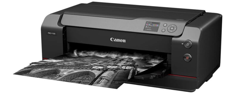 A Canon Pro-1000 color printer, with a sleek black design, is in use, printing a black-and-white photograph of a cathedral with dramatic clouds. The photo is emerging from the paper tray situated at the front of the printer.