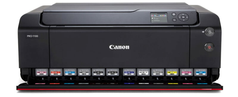 A Canon PRO-1000 professional printer with a sleek black design is shown. It has multiple ink cartridges visible at the front bottom, and a small display screen with buttons on the top right. The Canon logo is prominently displayed in the center.