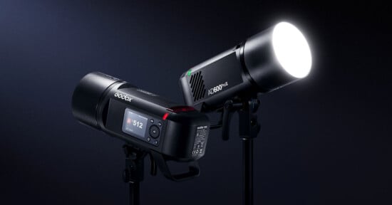 Two professional studio lights are displayed against a dark background. The light on the right emits a bright white light, while the light on the left features a visible control panel with a display reading "312." Both lights are mounted on stands.