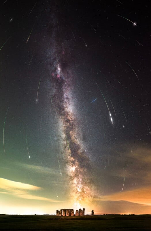 A stunning view of Stonehenge at night with the Milky Way galaxy visibly arching overhead. Star trails streak across the sky, creating a captivating celestial scene over the ancient stone circle.