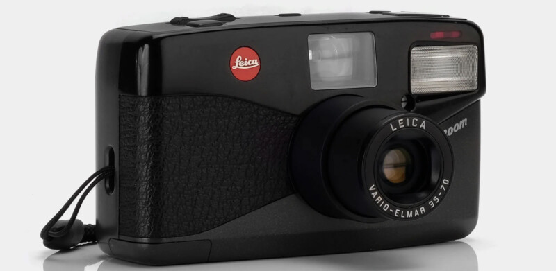 A black Leica compact camera with a textured grip, large viewfinder, built-in flash, and branded lens reading "Leica Vario-Elmar 35-70mm." The red Leica logo is visible on the top left corner. A wrist strap is attached on the left side of the camera.