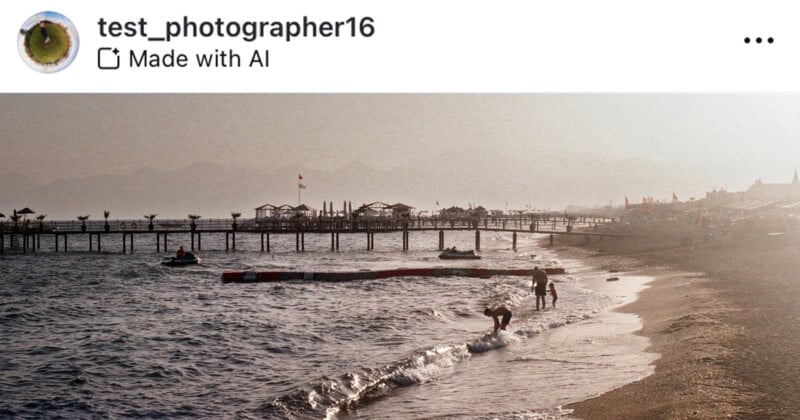 A beach scene in the early evening light with gentle waves reaching the shore. People are seen wading in the shallow water and enjoying the beach. A pier extends over the water, with some structures and flags visible. Hazy mountains are in the background.