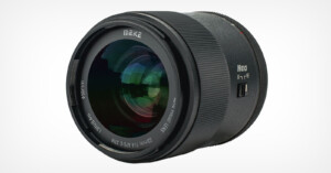 A large camera lens with a sleek black exterior. The lens is labeled "MEKE" and features various specifications, including "55mm," "Auro High Definition," and "F1.4." The lens surface reflects light, and there are fine grooves for grip.