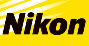 The image displays the Nikon logo, which consists of the word "Nikon" in bold black letters on a yellow background with three white diagonal stripes at the top left corner.