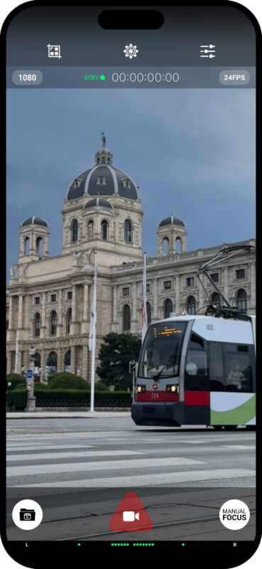 A smartphone screen shows a video recording interface with a tram passing in front of an ornate and historic building under a cloudy sky. Various icons, including zoom controls, 24FPS, and a manual focus button, are visible on the screen.