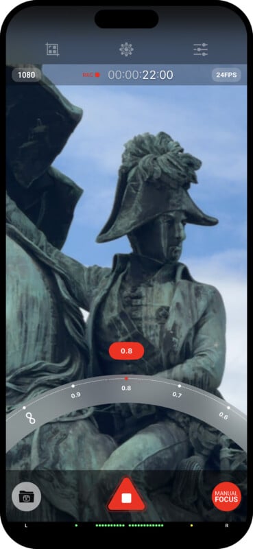 A smartphone screen shows a recording of a historical statue of two soldiers in period uniforms, one wearing a tall hat. The screen displays recording options, including resolution, exposure, and focus controls, with a red record button at the bottom center.