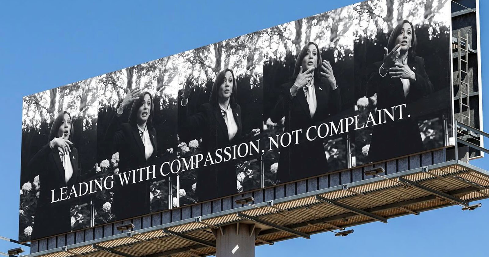 A large billboard displays a black-and-white photo series of a woman speaking expressively. The text on the billboard reads, "LEADING WITH COMPASSION, NOT COMPLAINT." The background includes trees and light shining through the leaves.