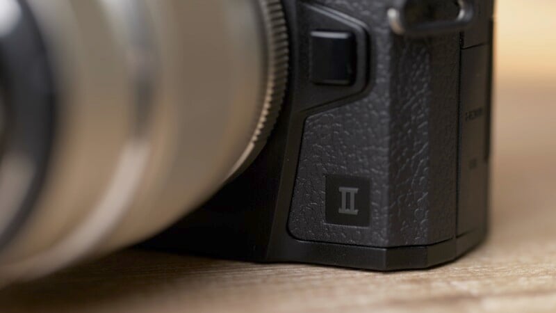 Close-up shot of a camera with focus on the textured black grip. The Roman numeral "III" is visible near the base of the camera body, indicating it is a model III version. The camera's lens mount and a portion of the lens are also partially visible.