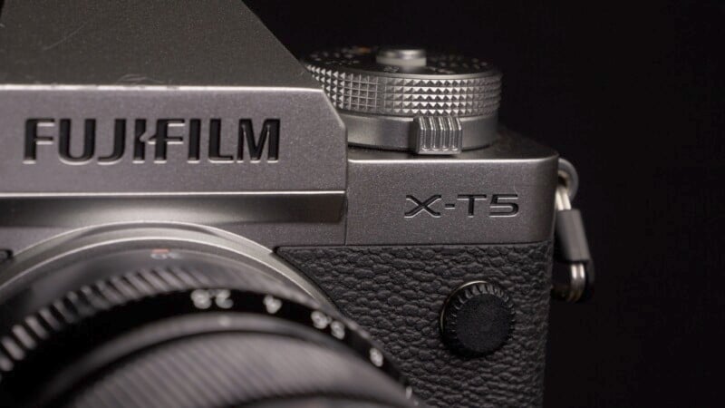 Close-up of a Fujifilm X-T5 camera, highlighting the X-T5 model name and the Fujifilm logo. The textured surface and a portion of the lens are visible, showcasing the details of the camera's design.