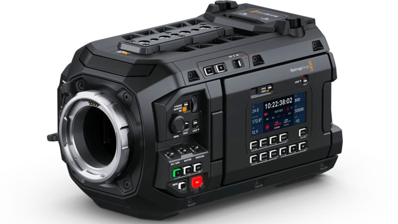 A digital cinema camera with a black, rugged design. It features multiple buttons and a touchscreen display on the side showing settings and information. The lens mount is prominently displayed at the front, and various connection ports are visible.