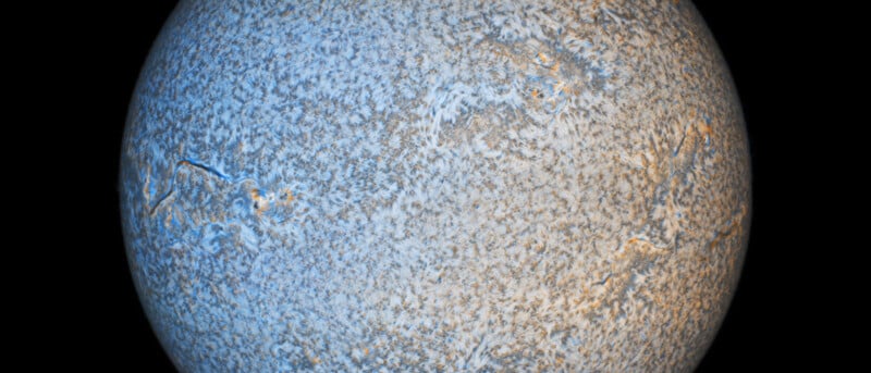 A high-resolution close-up image of the Sun, showcasing its textured surface covered in swirling patterns and structures. The overall color scheme is predominantly blue and white with hints of orange and grey, highlighting the Sun's dynamic activity. The background is black.