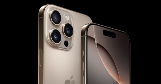 Close-up view of the gold-colored iPhone 15 Pro showing its rear camera system with three lenses and flash, and a partial view of the front screen with a dynamic island at the top. The background is black, highlighting the phone's sleek design.