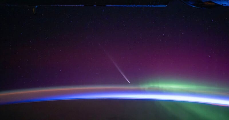 A stunning view from space captures a comet with a bright tail streaking through a star-filled sky. Below, an ethereal display of auroras in green and purple hues arcs over the curved horizon of Earth, where the atmosphere glows with a gradient of blue and orange.