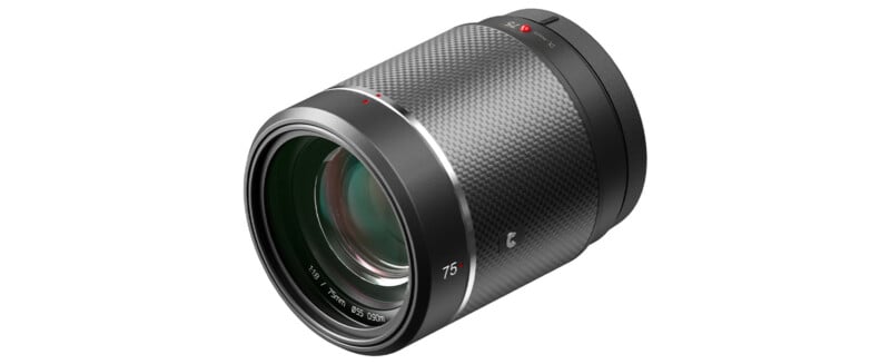 A black camera lens with a textured grip and a red dot marker near the mount is positioned on a white background. The lens has a greenish tint on the glass and markings indicating a focal length of 75mm.