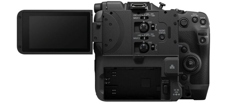 A digital camera viewed from the back with various buttons and dials visible. The camera has a flip-out LCD screen on the left side, which is currently extended. The control panel on the right includes audio input options and a battery compartment at the bottom.