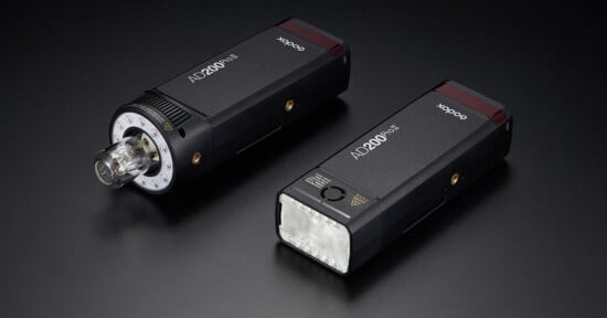 Two Godox AD200Pro portable flash units are displayed on a dark surface. One unit is shown with a bare bulb head, while the other features a rectangular LED head. Both flashes are prominent and accompanied by "AD200Pro" and "Godox" branding on their bodies.