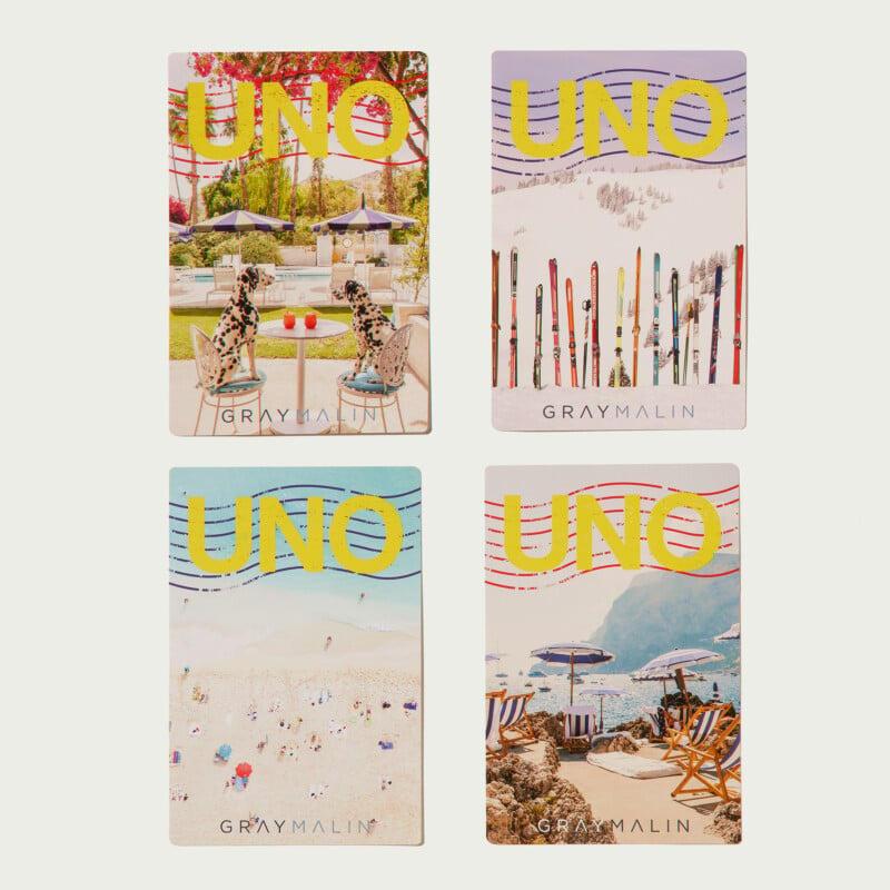 Four UNO card designs by Gray Malin. Top left card shows a poolside scene with leopard figures on chairs. Top right card depicts skis stuck in snow. Bottom left card features a beach scene with umbrellas. Bottom right card shows beach chairs at a rocky shore.