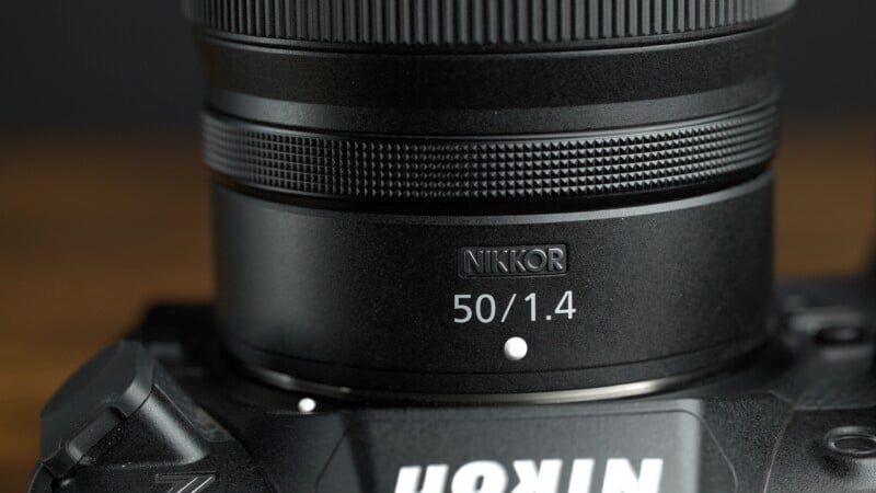 Close-up of a Nikon camera with a Nikkor 50mm f/1.4 lens attached. The focus is on the lens, showing detailed text and markings, while the lower part of the camera body is also visible.