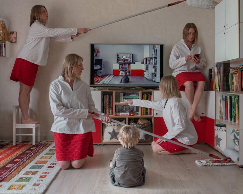 A young child sits on the floor facing a TV, surrounded by five identical women wearing white shirts and red skirts. Each woman is engaged in different activities, including dusting, cleaning the floor, using a phone, and holding a mop handle pointed at the TV.