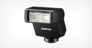 A black external camera flash unit with a rectangular flash head and the brand name "Pentax" printed on the front. The unit has a swivel joint at the base for attachment to a camera. The background is plain white.