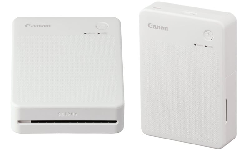 Two white Canon SELPHY compact photo printers are shown. One printer is positioned horizontally, displaying its front slot for photo output, while the other is positioned vertically, showing control buttons and indicator lights on the top surface.