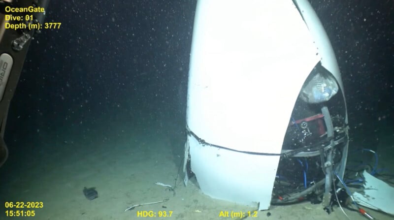 Underwater footage showing the wreckage of a white submersible vehicle with OceanGate branding, partially buried in the deep ocean. Visible details include a busted light, exposed wiring, and broken parts. Displayed data shows depth at 3777 meters and date as 06-22-2023.