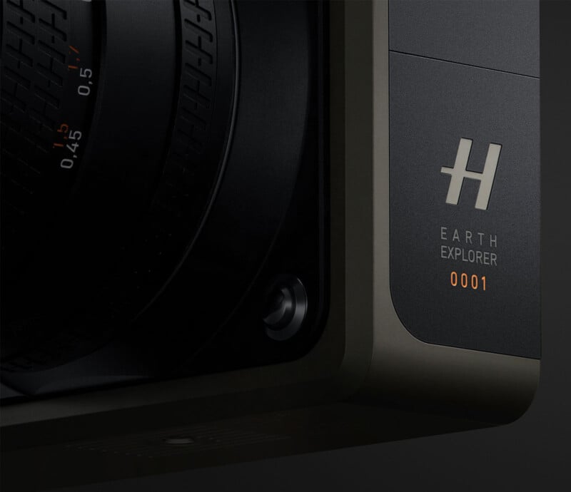 Close-up of a camera lens with intricate detailing, engraved with the text "EARTH EXPLORER 0001" in orange, and featuring a "H" logo above the text. The background is dark, highlighting the professional, high-end design of the camera.