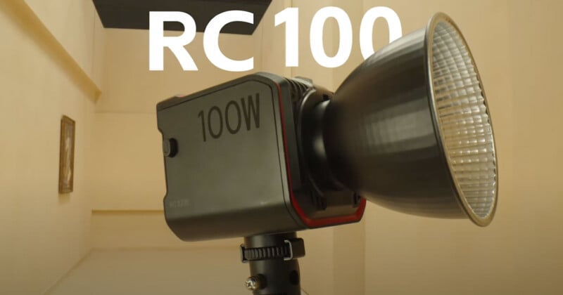 A close-up image of an LED studio light labeled "100W" mounted on a tripod, with the large reflective dish facing right. The background consists of beige-colored walls and a small framed picture. The bold text "RC 100" is prominently displayed at the top.