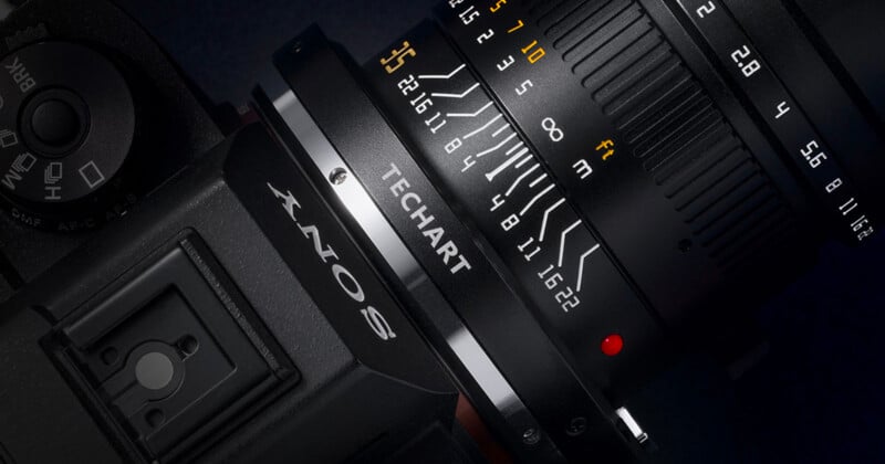 Close-up of a camera with a lens attached, showing detailed focus and aperture markings. The lens displays a brand name "TECHART" and distance indicators. The camera body has part of the "SONY" logo visible. The image emphasizes the technical details of the equipment.