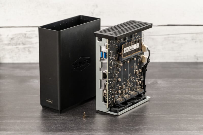 An open computer hardware device with its casing removed is shown. The device features an exposed circuit board with various electronic components, ports, and connectors. The casing beside it is black and labeled "Thermal Master." A single screw lies on the surface.