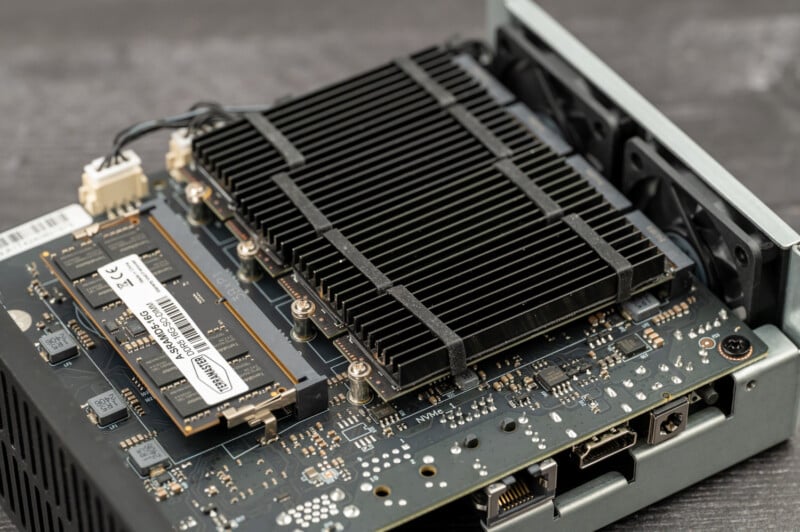 A close-up photograph of the interior of a computer showcasing a motherboard with various components including a large black heatsink, RAM module, and other circuitry. The components are neatly arranged, and some wiring is visible in the background.