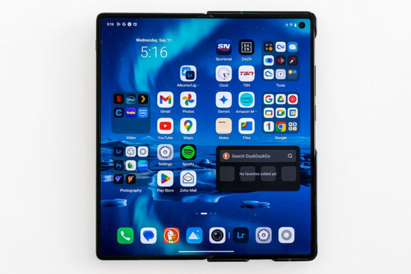 A foldable smartphone with an unfolded screen displays various app icons, including social media, productivity, streaming, and utilities. The screen also shows the time (5:16), date (Wednesday, Sept 11), a notification, and a search bar at the bottom.