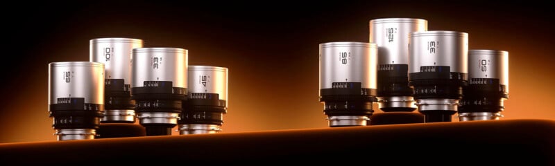 A lineup of camera lenses displayed against a glowing orange background. The lenses are silver with black rings, arranged in a staggered formation, showcasing varying sizes and focal lengths. The overall presentation has a sleek and professional appearance.