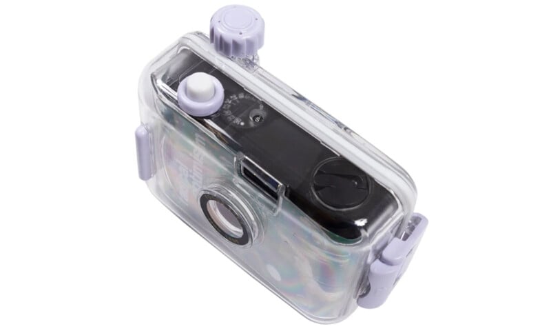 A compact black camera enclosed in a transparent, hard plastic, waterproof case with purple buttons and knob. The case features a large lens cover and is designed for underwater photography.