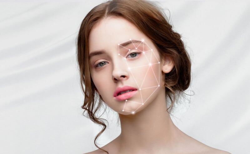 A young woman with light skin and brown hair is looking at the camera. She has a neutral expression. A geometric pattern of lines and points is superimposed over her face, suggesting facial recognition technology. The background is a plain, soft white.