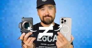 A bearded man wearing a black cap and a black shirt is holding a camera in his left hand and a smartphone in his right hand. A white "not equal to" symbol is overlaid between the camera and the smartphone. The background is a blue gradient with a pixelated pattern.