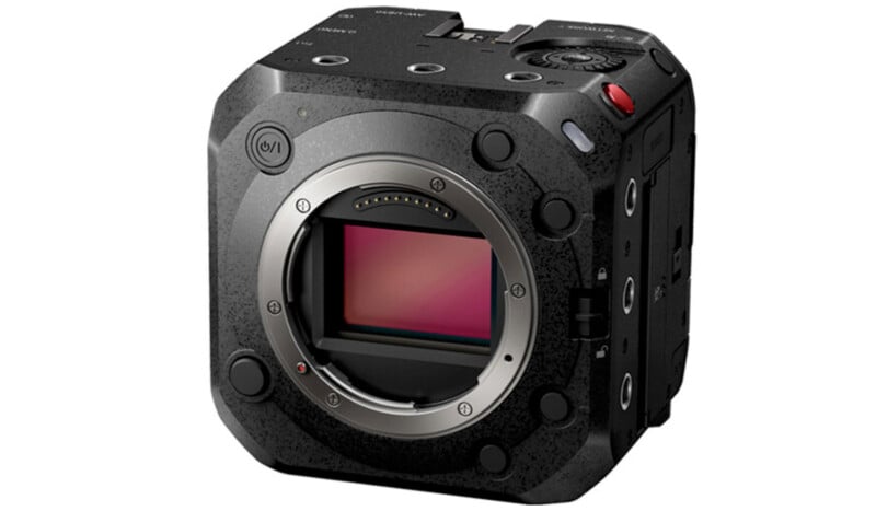 A black, cube-shaped digital camera body with multiple control buttons on the side, a large central lens mount, and a viewfinder on top. The camera has a rugged design and no lens attached, revealing the sensor inside the lens mount.