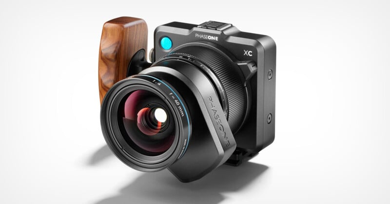 A high-end digital camera with a wooden grip is shown against a white background. The camera features a large lens, labeled "Phase One" with "XT" prominently displayed at the top. The design is sleek with a combination of black and wooden elements.