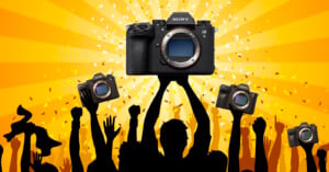 A crowd of silhouetted people raise their hands and Sony Alpha cameras in celebration. The central figure holds up a Sony Alpha 9 camera against a yellow background with confetti and radiant light beams.