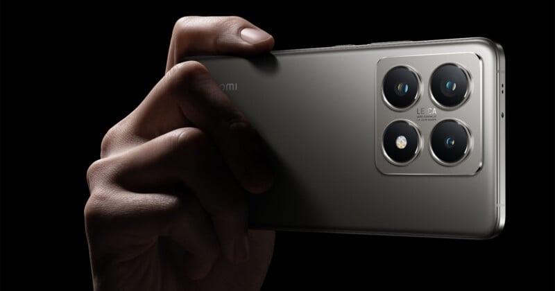 Close-up image of a hand holding a sleek, modern smartphone with a quad-camera setup on the back. The metal finish of the phone is highlighted against a black background, showcasing the sophisticated design and prominent camera lenses.