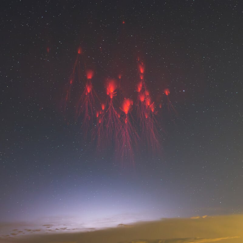 A night sky filled with stars features bright red lightning sprites, resembling jellyfish, above a dimly lit horizon. The lower sky is a gradient from dark to soft yellow with scattered clouds.