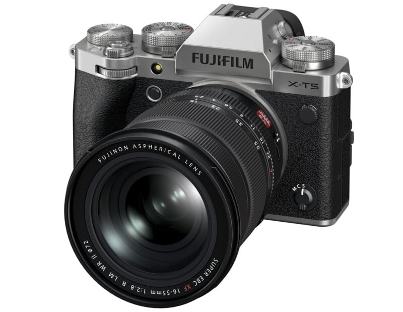 A Fujifilm X-T5 camera with a large Fujinon aspherical lens attached. It features a retro design with silver and black colors, several dials on top, and a textured grip.