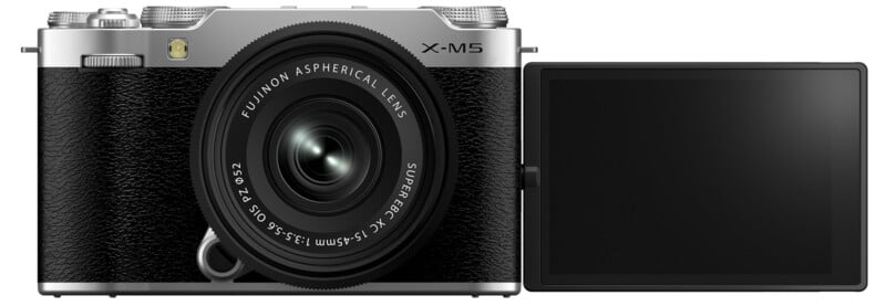 A silver and black digital camera with an open LCD screen on the right side. The camera has a prominent lens labeled "Aspherical Lens." The screen is facing outward, showing no image.