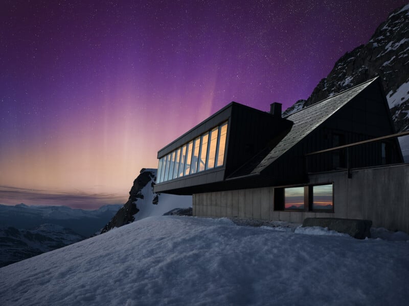 A modern cabin with large windows is perched on a snowy mountainside. The sky is filled with vibrant purple and pink hues, suggesting a sunset or sunrise, and snow-covered peaks are visible in the distance.