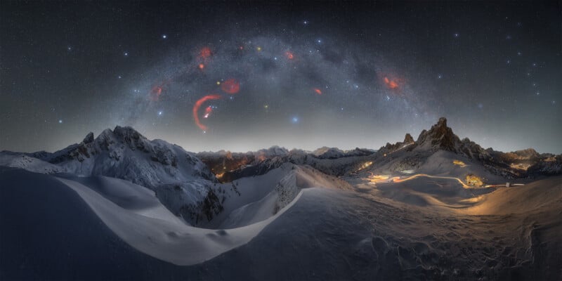 A breathtaking night sky panorama above snow-covered mountains, featuring a stunning Milky Way arch. The snowy landscape is illuminated by the soft glow of scattered mountain huts, with rugged peaks in the distance and stars twinkling brightly above.